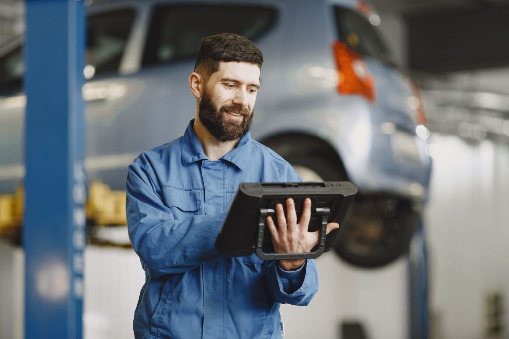 Kfz-Mechatroniker steht in der Werkstatt und erfasst einen Auftrag auf dem Tablet